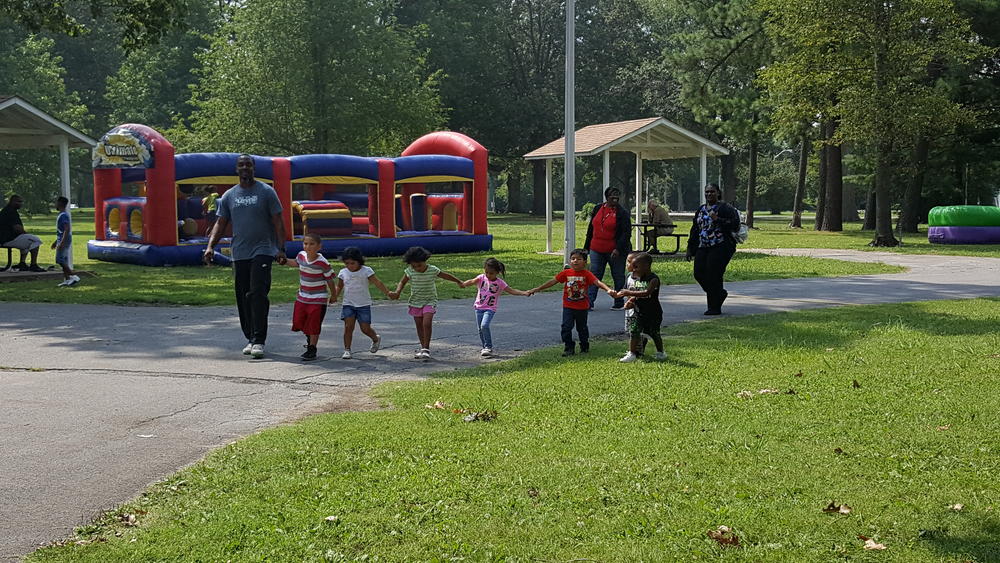 An adult walking with a group of small children holding hands at a park