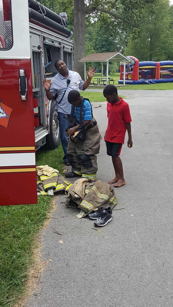 A fireman letting two children put on fire gear