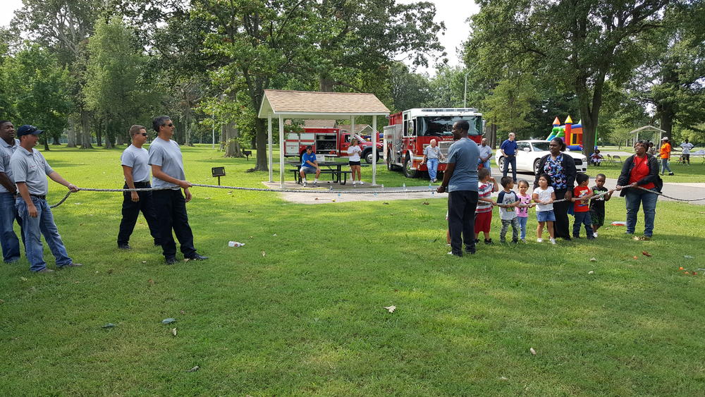 Children and adults playing tug-of-war with law enforcement officers at a park
