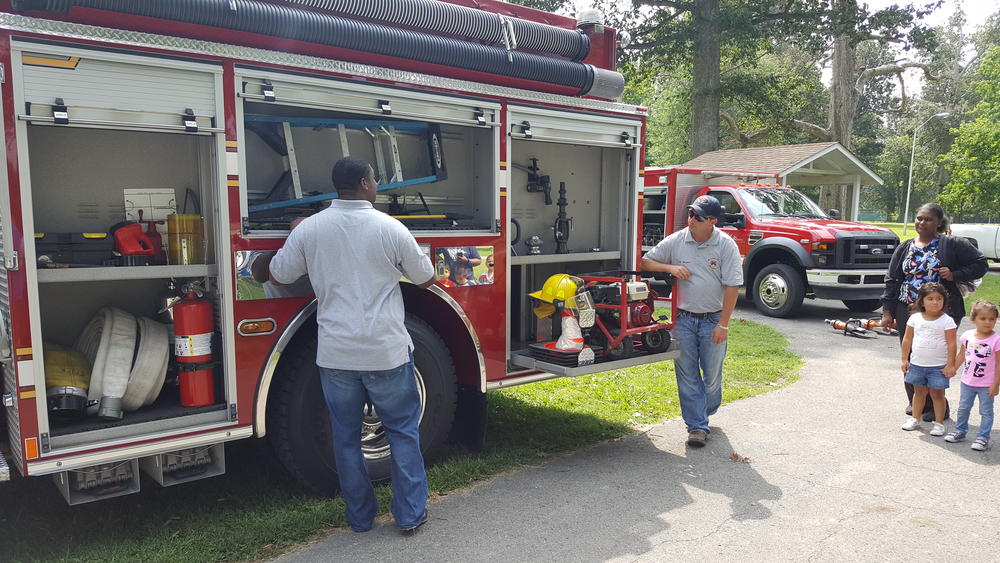 Two men showing adults and children a firetruck at a park