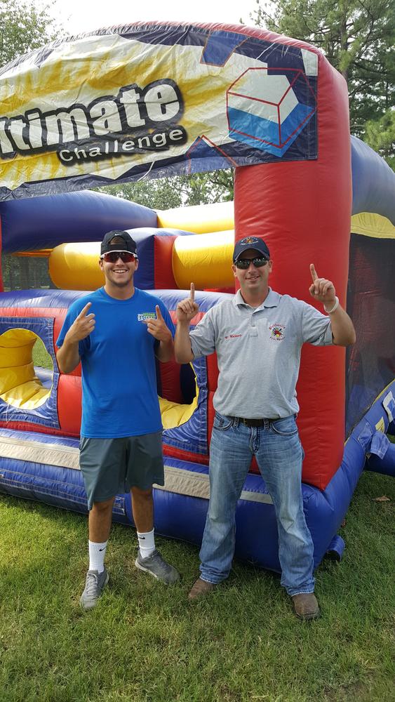 Two men holding up the number one sign with their hands in front of a blowup playhouse