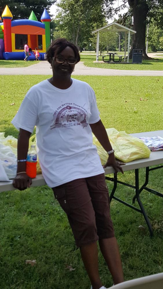 A woman smiling while standing next to tables with stacks of shirts