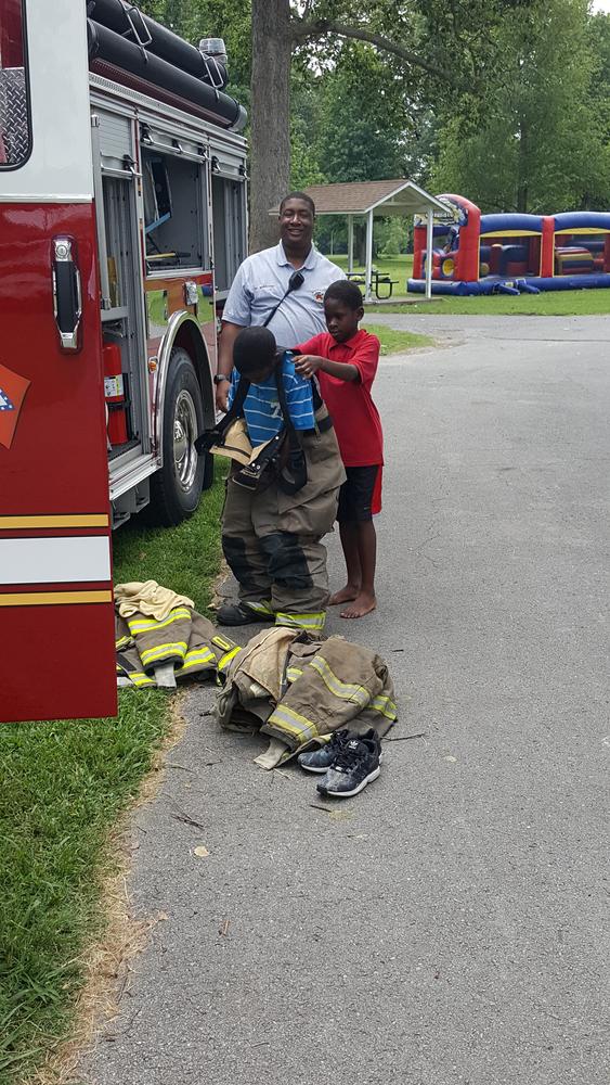 A fireman letting two children put on fire gear