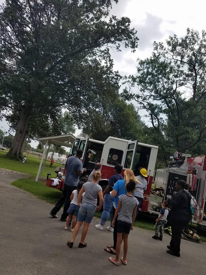 Two firemen showing a group of children a fire truck and equipment