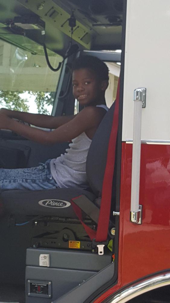 A child sitting in the driver's seat of a firetruck and smiling at the camera