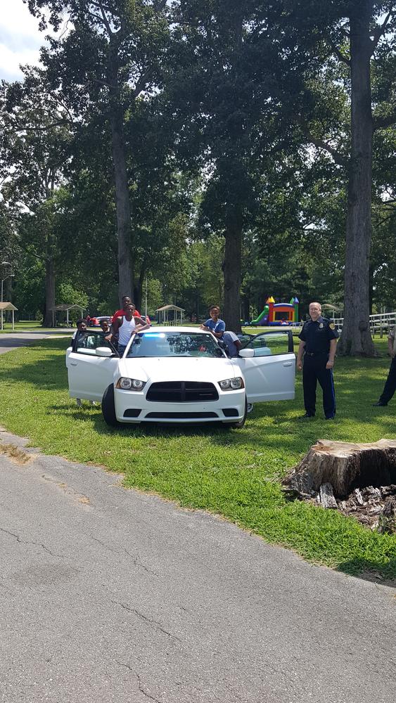 Adults and children standing next to a police car with an officer in front